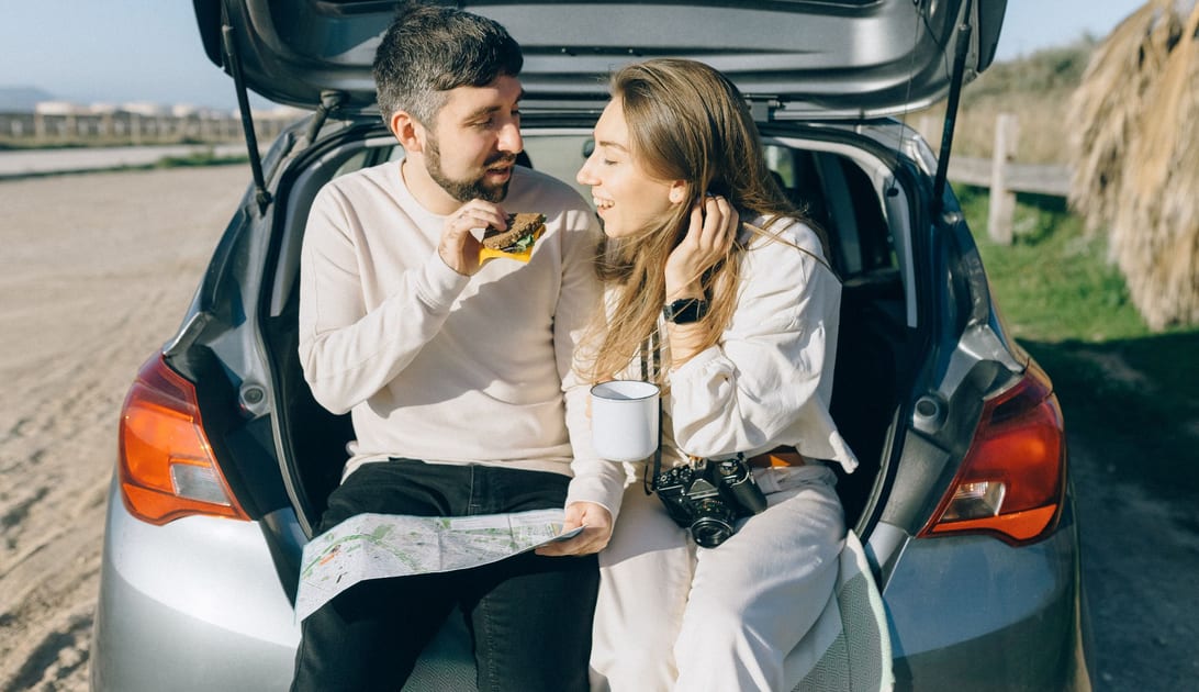 Casal fazendo um lanche no porta-malas do carro durante parada em viagem de carro