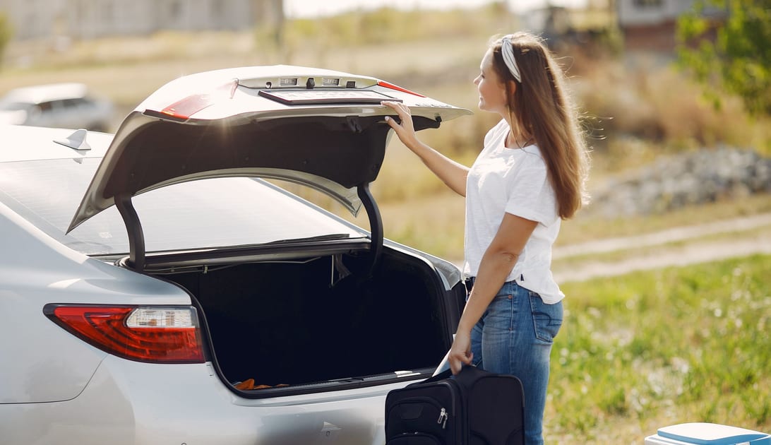Viajante com bolsa de viagem abrindo o porta-malas do carro alugado