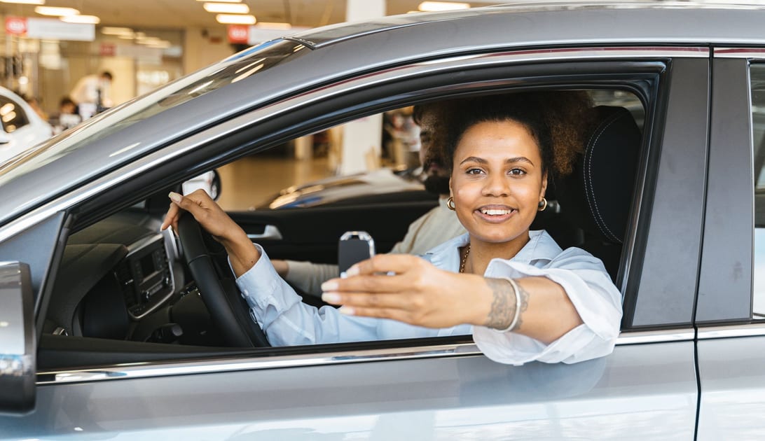 Cliente sorridente ao volante mostrando a chave do carro alugado