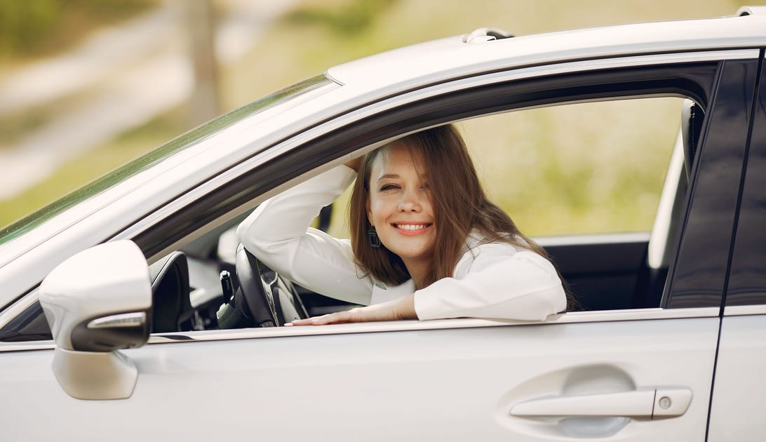 Motorista tranquila e sorridente ao volante, com paisagem verde ao fundo